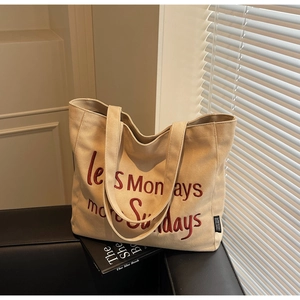 Close-up of beige canvas tote with red less Mondays more Sundays embroidery on a leather sofa