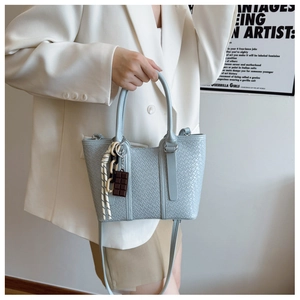 Détail d'un sac cabas tissé bleu clair avec breloque chocolat et pendentif en corde