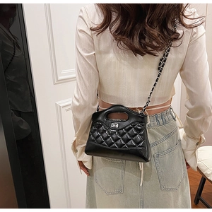 Detail of black quilted leather handbag with silver metal turn-lock and chain strap