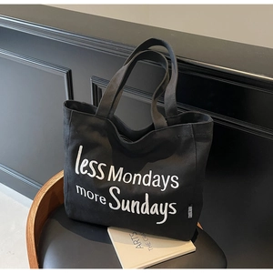 Detail shot of black canvas tote bag with white less Mondays more Sundays text