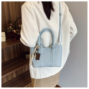 Détail du sac à bandoulière bleu clair avec texture tissée et charm porté par un modèle