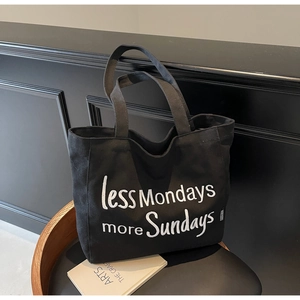 Detail of black canvas tote bag with white less Mondays more Sundays print on a chair