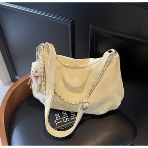Close-up of pale yellow Hobo bag with metal chain decoration and white bear plush charm