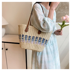 Détail d'un sac cabas en paille tressée avec motifs bleus et anses en cuir marron