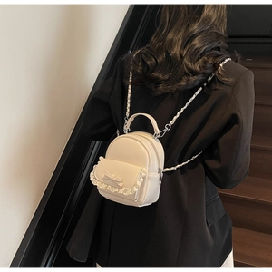 Detail of cream mini backpack with lace trim and bow on a model in black blazer