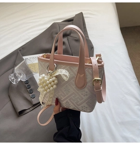 Detail of pink floral tote with pearl heart charm and leather strap on a bed