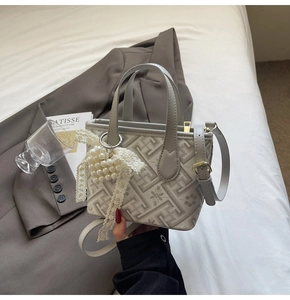 Detail of grey geometric tote bag with large pearl lace bow charm on bed