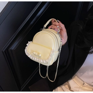 Detail of yellow PU leather mini backpack with lace trim and bow accent held by hand