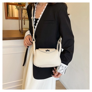 Detail of creamy white leather crossbody bag showing metallic twist lock and pebbled texture