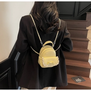Close-up of yellow mini backpack with lace lace-up bow and silver chain straps detail