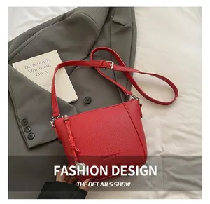 Détail d'un sac bandoulière rouge avec texture litchi, fermeture à gland et sangle