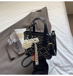 Detail of geometric embroidery tote bag with pearl lace bow and black leather handle