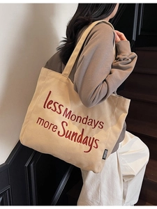 Minimalist beige canvas tote bag with red Sunday embroidery worn on shoulder