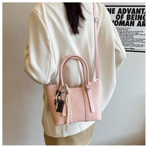 Détail d'un sac bandoulière rose tissé avec breloque chocolat sur un mannequin chic