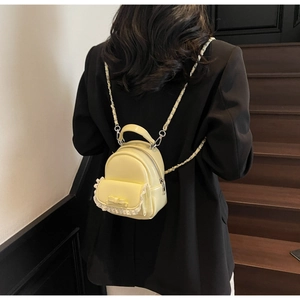 Close-up of mini yellow backpack featuring lace trim, bow detail, and chain strap