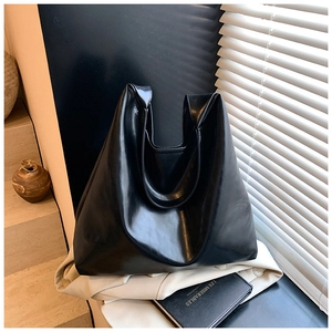 Detail of a large black glossy faux leather tote bag on a trench coat with soft lighting