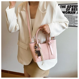 Détail du sac bandoulière tissé rose clair avec chaîne décorative et nœud rayé élégant