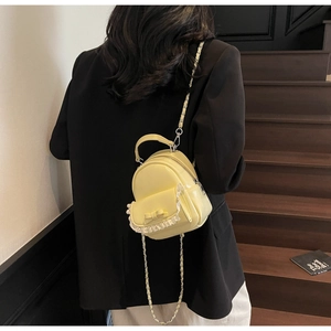 Detail of yellow glossy mini backpack with bow decoration and metal chain strap