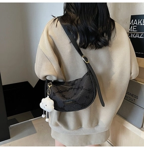 Close-up of black crescent crossbody bag with 3D texture and white cloud plush charm