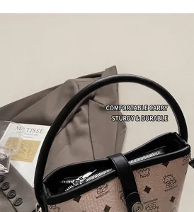 Detail of beige lychee leather bag with dinosaur print and black cylindrical handle