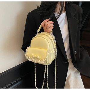 Detail of yellow mini backpack with lace trim, bow decoration and silver chain strap