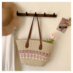 Détail du sac cabas en paille tissé avec accents violets suspendu à un crochet