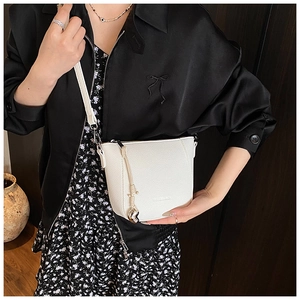 Détail du sac seau blanc à motif litchi avec breloque cœur doré et ornement de gland