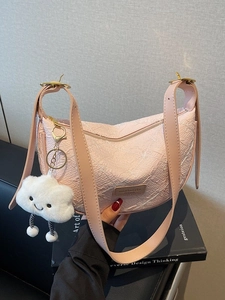 Pink textured dumpling bag with plush cloud charm on a black book background