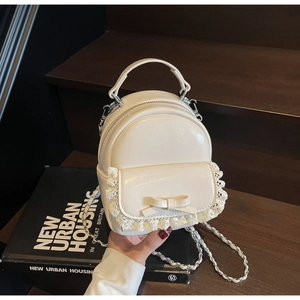 Detail of cream white mini backpack featuring lace trim and bow with silver chain strap