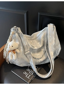 Sac hobo argenté métallisé avec peluche ours sur un fauteuil en cuir noir