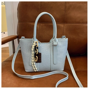 Détail d'un sac à main tissé bleu clair avec des breloques chocolat sur canapé en cuir