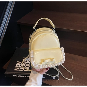 Detail of cream yellow glossy mini backpack featuring lace trim and bow knot detail