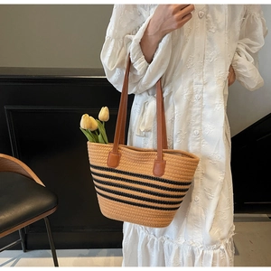Detail of woven straw tote bag with black stripes and leather shoulder straps for beach