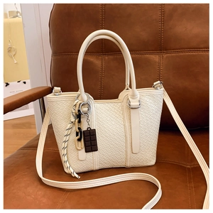 Détail du sac bandoulière blanc avec breloques artistiques sur un canapé en cuir