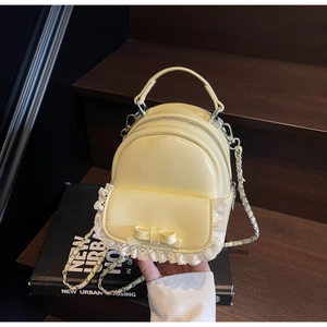 Detail of cream yellow mini backpack with delicate white lace trim and leather bow