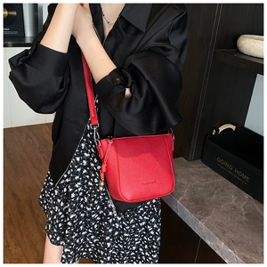Détail d'un sac seau rouge en cuir grainé avec pompons porté par un mannequin