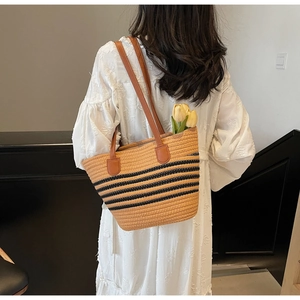 Detail of bohemian straw tote bag with black stripes and brown leather shoulder straps