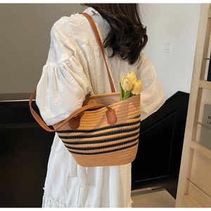 Detail of woven straw tote bag with black stripes and brown leather straps on a white dress