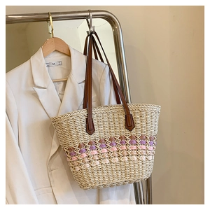 Détail d'un sac cabas en paille tressée avec bandes colorées et poignées en cuir marron