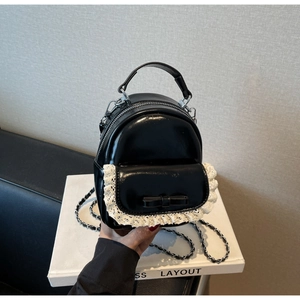 Detail of black patent leather mini backpack with white lace trim and bow accents