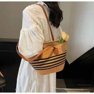 Detail of woven straw tote bag with black stripes and brown leather straps on a model