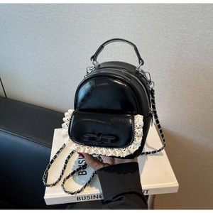 Detail of black faux leather backpack featuring white lace trim and bow accent
