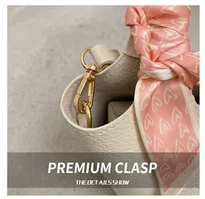 Close-up of white lychee grain leather handbag with gold metal hook and heart silk scarf