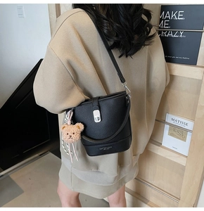 Close-up of black lychee leather bucket bag with silver buckle and plush bear charm