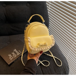 Detail of light yellow mini backpack with lace trim, bow, and gold chain strap on chair
