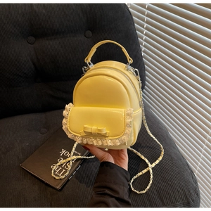 Mini yellow backpack with lace lace and bow detail held in hand with silver chain strap