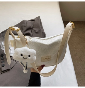 Detail of white textured dumpling bag with leather strap and cloud plush charm