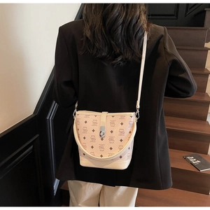 Detailed view of beige bucket bag with bear print and metal clasp worn over a black blazer