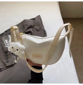 Detail of white textured crescent bag with adjustable strap and plush cloud charm accessory