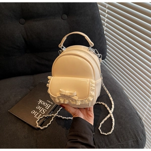 Detail of creamy white mini backpack featuring lace trim, bow, and silver chain strap
